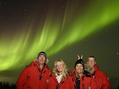 Family of 4 stand together in red coats with the aurora borealis behind them