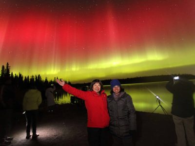 2 women pose for picture with red and green aurora behind them