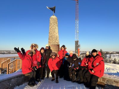 Large group of people in red winter jackets at Pilots Monument with a blue sky behind them